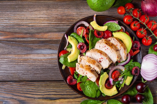 Ensalada saludable hecha de filete de pollo a la parrilla, espinacas, aguacate, tomates y bayas de cereza para el almuerzo o la cena de dieta