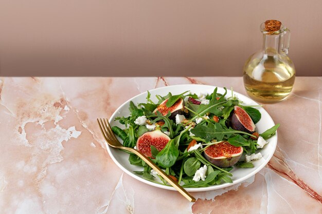 Ensalada saludable con higos, rúcula, queso feta y aceite sobre fondo de mármol beige rosa Ensalada de higos de otoño