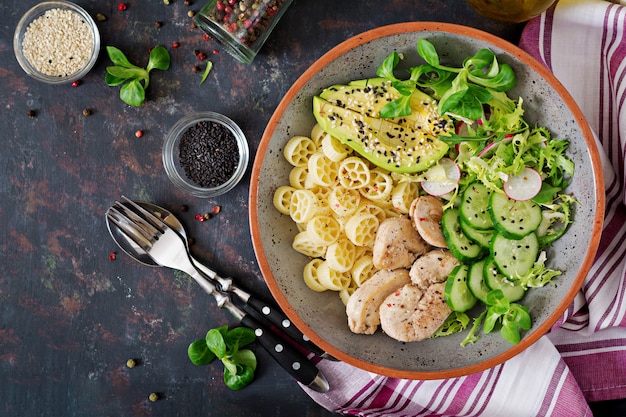 Ensalada saludable con pollo, aguacate, pepino, lechuga, rábano y pasta en la mesa oscura. Nutrición apropiada. Menú dietético Cena. Endecha plana. Vista superior