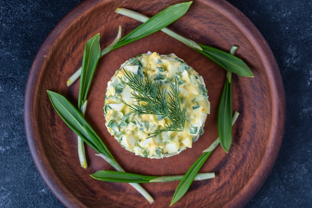 Foto ensalada saludable de puerro salvaje verde, huevo escalfado y crema agria en placa, de cerca. ensalada de ajo silvestre con huevos duros