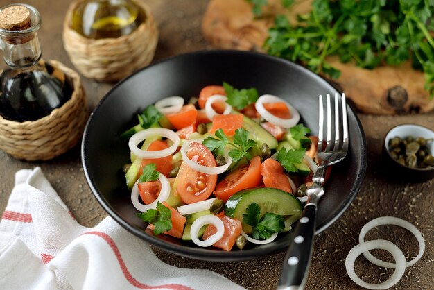 Ensalada saludable de tomates cherry, pepino, apio, cebolla, alcaparras y perejil con salmón salado.