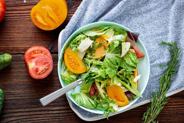 Ensalada saludable de verduras frescas, hierbas y tomates sobre un fondo de madera.