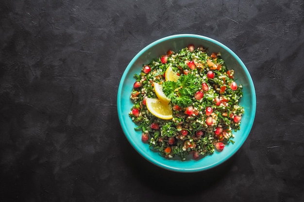 Ensalada tabulé con cuscús en un recipiente sobre la mesa negra. Ensalada vegetariana levantina con perejil, menta, bulgur, tomate.