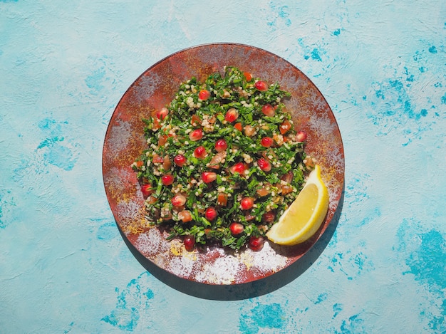 Ensalada tabulé con cuscús en un tazón rojo sobre mesa rústica azul