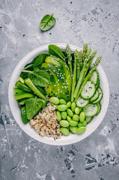 Ensalada de tazón de buda vegetariana verde saludable con verduras frescas y quinua, espinacas, aguacate, espárragos, pepino, frijoles de edamame con semillas de sésamo sobre fondo gris Vista superior