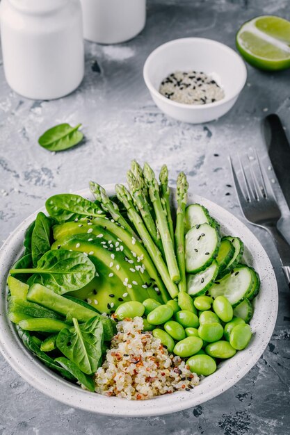 Ensalada de tazón de buda vegetariana verde saludable con verduras frescas y quinua, espinacas, aguacate, espárragos, pepino, frijoles de edamame con semillas de sésamo sobre fondo gris