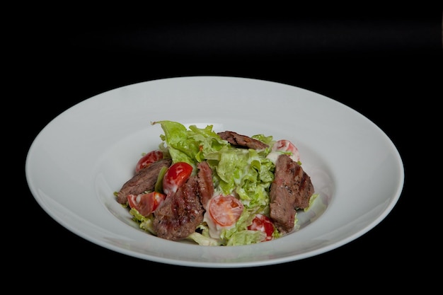 Ensalada de ternera con grandes rodajas de ternera y verduras frescas en un plato de fondo negro