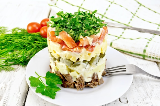 Ensalada de ternera, patatas cocidas, encurtidos, queso, tomate, perejil en el plato, servilleta, eneldo en el fondo tablas de madera clara