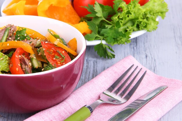 Ensalada de ternera en un tazón con verduras sobre fondo de madera