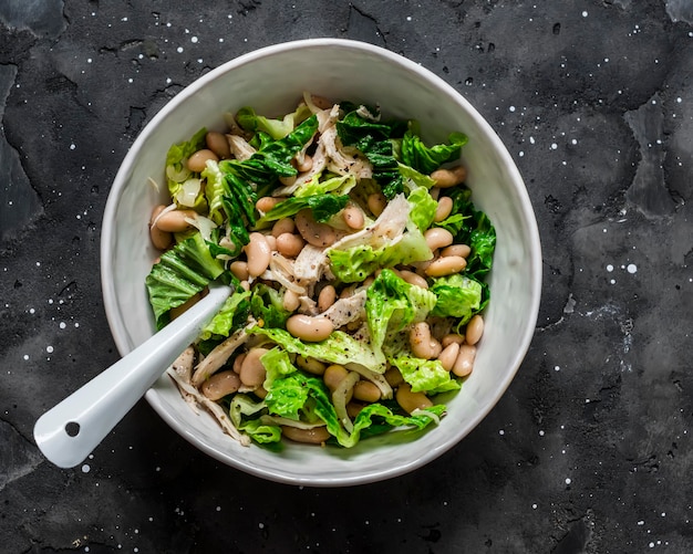 Ensalada tibia con frijoles, pechuga de pollo al horno, lechuga romana en una vista superior de fondo oscuro