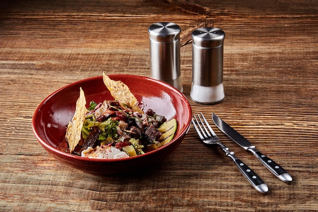 Ensalada tibia de frijoles de ternera, semillas de sésamo, huevo de pimienta de tomillo en un tazón de cerámica sobre una mesa de madera