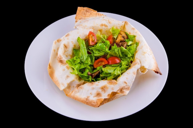 Ensalada tibia en pan de pita fino: ternera, champiñones, tomates cherry, mostaza de Dijon, coñac. Aislado sobre fondo negro