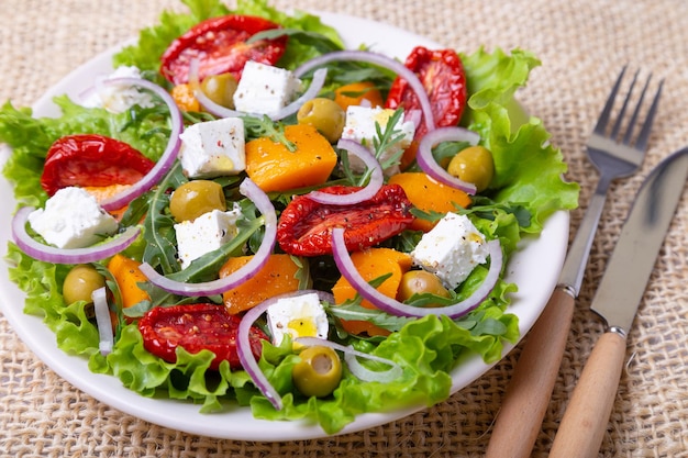 Ensalada tibia con queso feta de calabaza tomates secos aceitunas rúcula y cebolla roja Primer plano