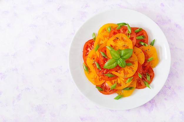 Ensalada de tomate amarillo y rojo con pesto de albahaca sobre un fondo claro.