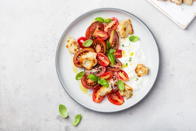 Ensalada de tomate, stracciatella, ciabatta y albahaca sobre un fondo claro