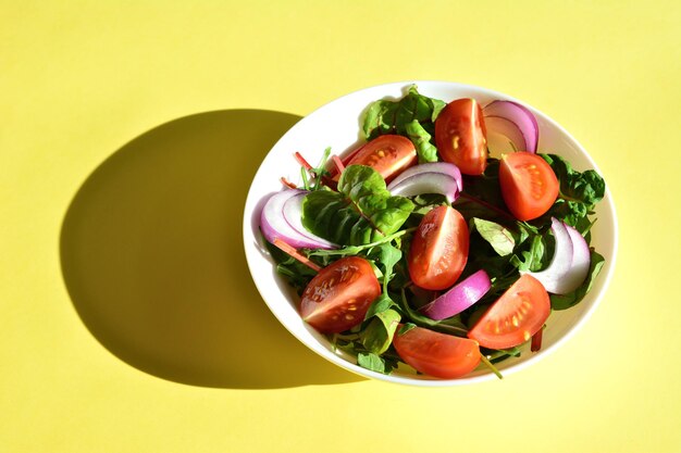 Ensalada con tomates cebolla roja y verduras de ensalada en tazón blanco sobre fondo amarillo