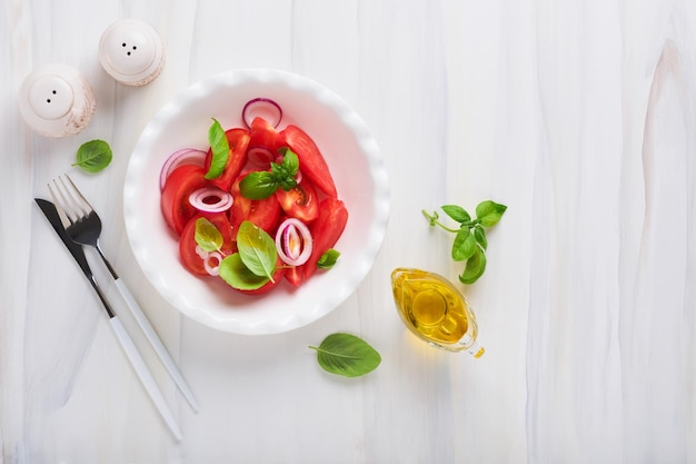 Ensalada de tomates frescos con hojas de albahaca, aceite de oliva y cebolla en un tazón blanco sobre fondo claro Dieta tradicional italiana o mediterránea Vista superior