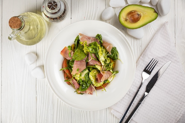 Ensalada con tomates mozzarella de Parma y verduras sobre un plato blanco y mesa blanca