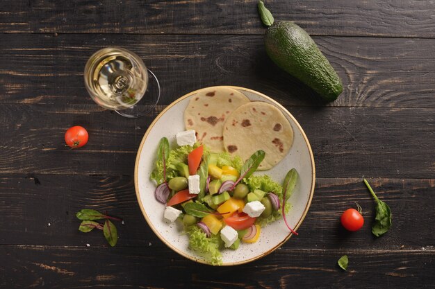 Ensalada con tomates, pepinos, pimientos, aceitunas y queso feta. Ensalada griega. en un plato de arcilla blanca sobre una mesa de madera