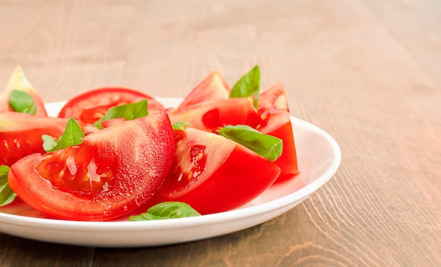 Ensalada de tomates picados y albahaca en un plato sobre una mesa de madera