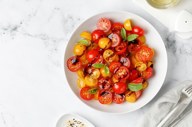 Ensalada con tomates rojos y amarillos cereza con salsa balsámica y albahaca en un plato blanco