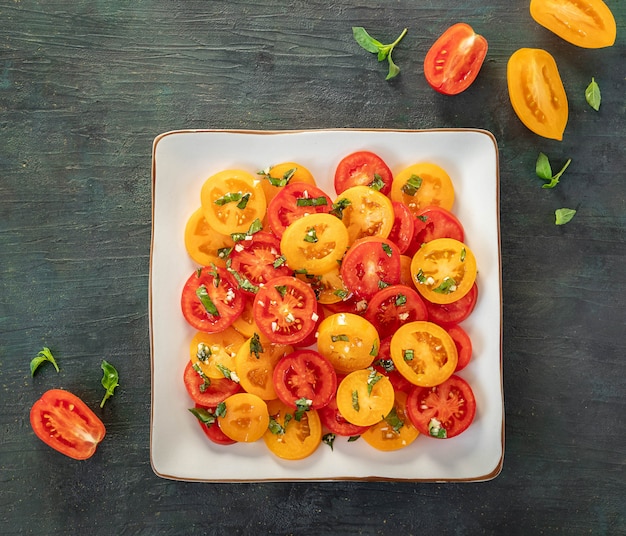 Ensalada de tomates rojos y amarillos frescos con albahaca sobre un fondo oscuro