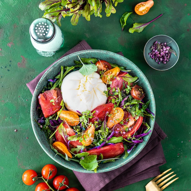 Ensalada con tomates, rúcula, queso burrata y microgreens sobre un fondo de piedra verde, vista superior, cuadrado