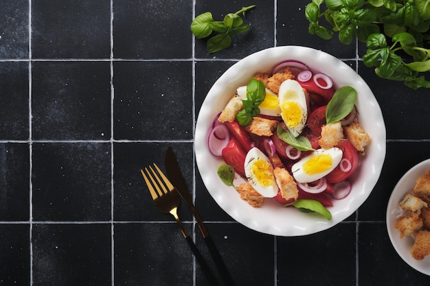 Ensalada toscana de panzanella Ensalada de tomates frescos con hojas de albahaca, huevos, aceite de oliva y cebolla en un tazón blanco sobre fondo negro antiguo Ensalada vegetariana de panzanella Comida saludable mediterránea Vista superior