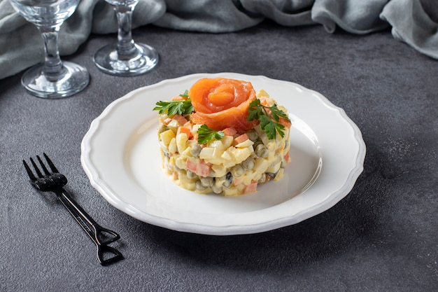 Foto ensalada tradicional rusa olivier con salmón salado sobre un fondo gris oscuro.