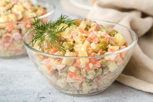 Ensalada tradicional rusa Olivier con verduras hervidas, en una ensaladera de vidrio sobre la mesa. Fondo gris, primer plano.