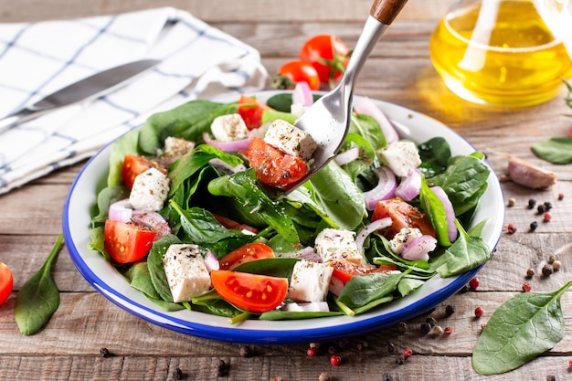 Ensalada vegana de primavera con espinacas, tomates cherry, espinacas baby, queso feta y cebolla roja sobre una mesa de madera rústica. Concepto de comida sana.