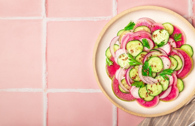 Foto ensalada vegana saludable con pepino de rábano sandía y cebolla roja sobre fondo de azulejo rosa vista superior