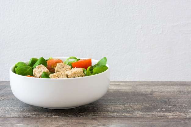 Ensalada vegana de tofu en un tazón con tomates y lechuga de cordero en la mesa de madera