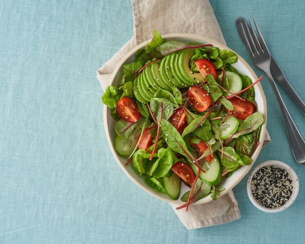 Ensalada vegana con tomates, pepinos, aguacate sobre mantel de lino azul. Comida mediterránea vegetariana, comida dietética baja en calorías, espacio de copia