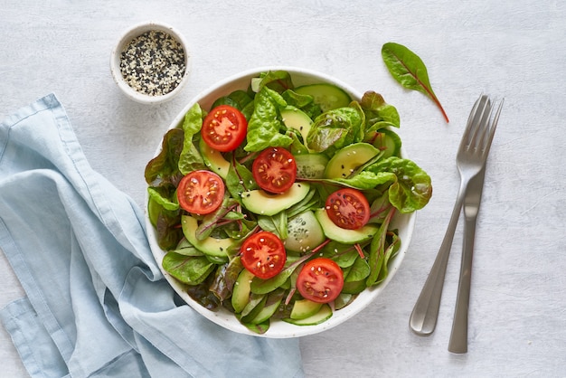 Ensalada vegana con tomates, pepinos, aguacate sobre mesa de hormigón gris pastel. Comida mediterránea vegetariana, comida dietética baja en calorías