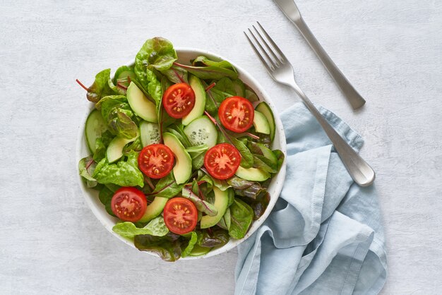 Ensalada vegana con tomates, pepinos, aguacate sobre mesa de hormigón gris pastel.