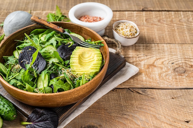 Ensalada vegana verde con mix de hojas verdes, aguacate y verduras. Fondo de madera. Vista superior. Copie el espacio.