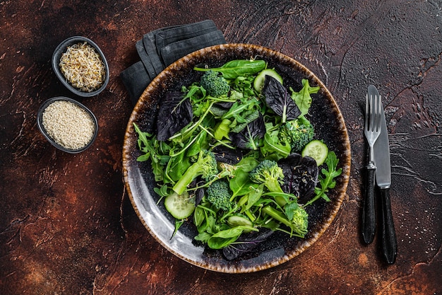 Ensalada de vegetales saludables con hojas frescas de rúcula, lechuga, espinacas para ensalada vegana. Fondo oscuro. Vista superior.