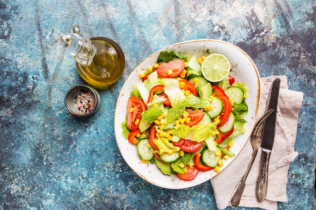 Ensalada de vegetales saludables de tomate fresco, pepino, lechuga y maíz en un plato, vista superior. Menú de dieta.