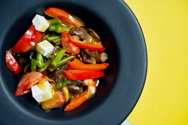 Ensalada vegetariana apetitosa y saludable con verduras a la parrilla, aderezo y queso en un recipiente negro sobre una superficie coloreada Vista superior de comida sabrosa