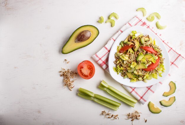 Ensalada vegetariana de apio, centeno germinado, tomates y aguacate sobre mantel de lino.