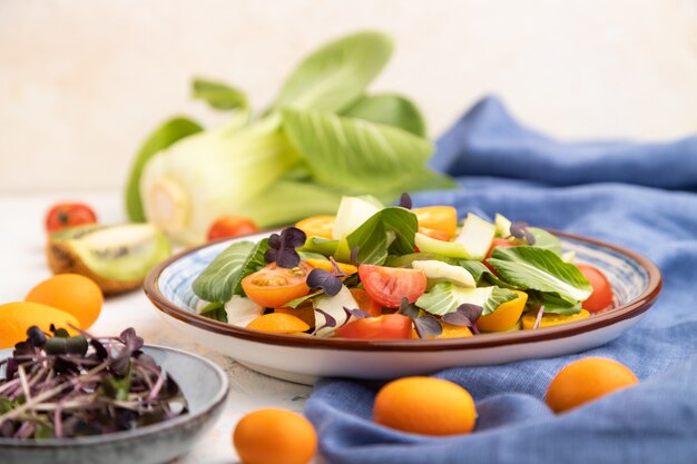 Ensalada vegetariana de col pac choi, kiwi, tomates, kumquat, brotes microgreen sobre una superficie de hormigón blanco. Vista lateral, enfoque selectivo.