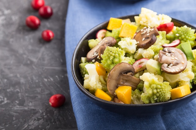 Ensalada vegetariana de col romanesco, champiñones, arándanos, aguacate y calabaza sobre una superficie de hormigón negro. Vista lateral, enfoque selectivo.