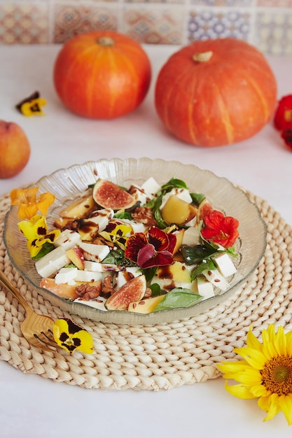 Ensalada vegetariana con feta flores comestibles higos melocotón albahaca sobre fondo de cerámica con girasoles y decoraciones de calabaza