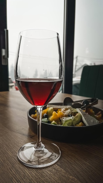 Foto ensalada vegetariana fresca con tomates, lechuga y queso en un plato oscuro y una copa de vino tinto