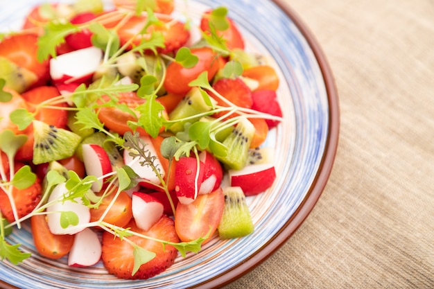 Foto ensalada vegetariana de frutas y verduras de fresa, kiwi, tomate, brotes microgreen sobre fondo de hormigón negro.