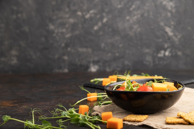 Ensalada vegetariana de tomates, calabaza, brotes de guisantes microverdes sobre hormigón negro