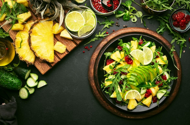 Ensalada vegetariana vegana con piña, rúcula, aguacate y cereza seca en un plato negro en la mesa de la cocina de piedra oscura, vista superior, alimentación saludable, dieta limpia, comida, pérdida de peso, concepto