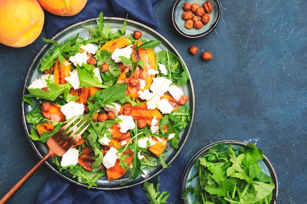 Ensalada de verano con melocotón a la parrilla con avellanas de queso suave y rúcula en el espacio de copia de la vista superior del fondo de la mesa azul