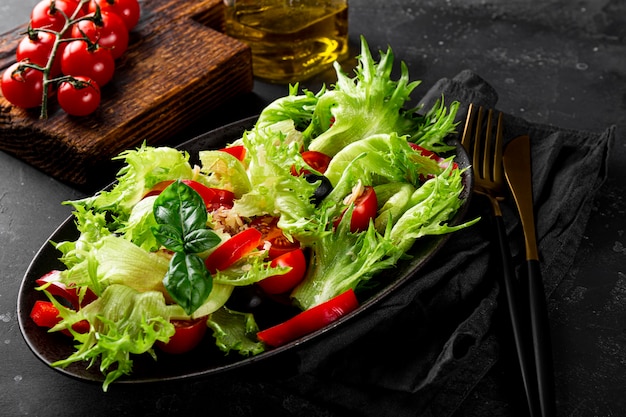 Ensalada de verano simple de lechuga, tomates con aceitunas y aceite de oliva en un primer plano de la placa negra.